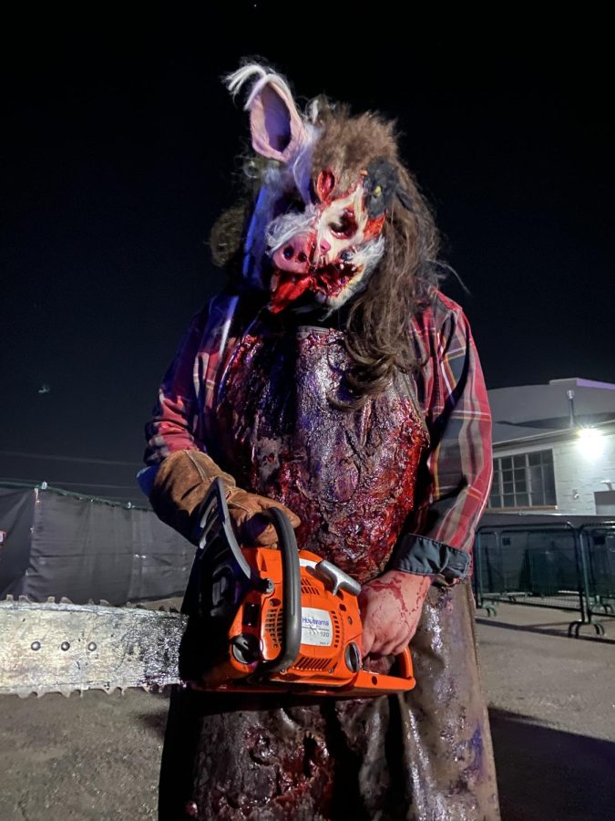 A bloody monster carries a chainsaw outside of a haunted house.