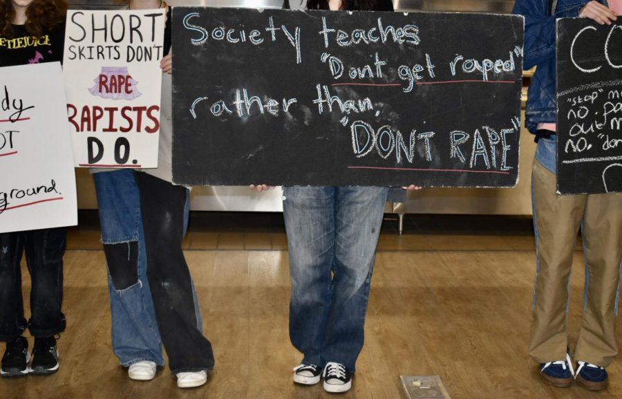 Students stand in the cafeteria holding protest signs to catch the attention of passerby. 